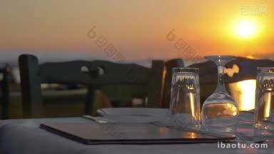 日落时分，露天餐厅的空桌子上摆着餐具和玻璃器皿，白色桌布上放着菜单